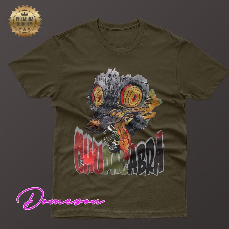 May include: Olive green t-shirt featuring a graphic of a creature with large yellow eyes and the word "CHUPACABRA" in red and gray. The shirt has a crew neck and short sleeves. A "Premium Quality" seal is in the upper left corner.