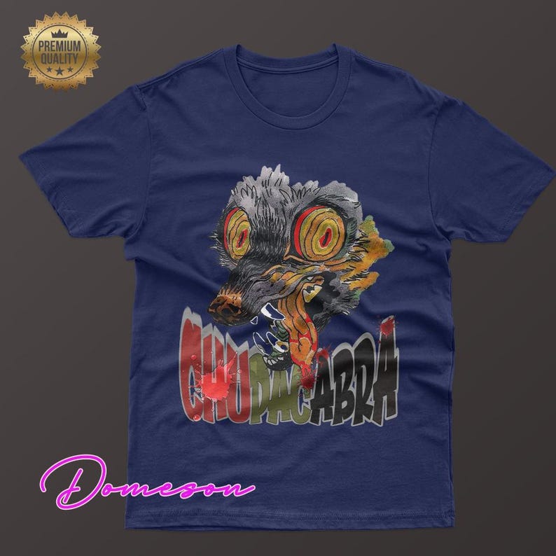 May include: Navy blue t-shirt featuring a graphic of a creature with large yellow eyes and the word "CHUPACABRA" in a graffiti-style font. The design includes red, gray, and orange colors. A "Premium Quality" seal is in the upper left corner.
