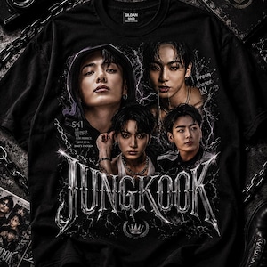May include: A black short-sleeved t-shirt featuring a graphic print of four portraits of Jungkook. The design includes metallic silver text reading JUNGKOOK, a crown icon, and the phrases Still Here and Dream Chaser, all set against a lightning background.