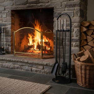 May include: A fireplace with a burning fire, a gold-framed screen, and a black metal tool set. A woven basket holds firewood, and a beige rug sits on the slate floor. The stone fireplace creates a warm, inviting atmosphere.