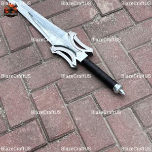 May include: A silver-colored sword with a decorative hilt and a black handle. The sword is lying on a brick surface. The text "BlazeCraftUS" is repeated across the image.
