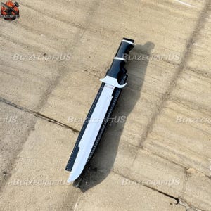 May include: A large, silver-bladed knife with a black and white handle, resting in a black sheath. The knife has the word "PREDATOR" on the blade. The sheath is black with white stitching.
