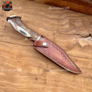 May include: A hunting knife with a deer antler handle and a brown leather sheath. The knife blade is silver, and the sheath has a decorative embossed pattern. The knife is designed for outdoor use.