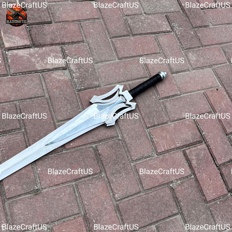 May include: A silver-colored sword with a black handle. The blade has a unique design with a decorative hilt. The sword is displayed on a brick surface. The text "BlazeCraftUS" is visible in the image.