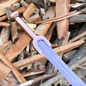 May include: A fantasy sword with a lavender blade and a gold-colored hilt. The sword is set against a backdrop of various pieces of wood. The sword's design is reminiscent of medieval weaponry.