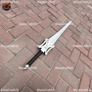 May include: A silver and black sword with a stylized hilt and a long, pointed blade. The handle is wrapped in black material. The sword is lying on a brick surface. The text "BlazeCraftUS" is visible in the image.