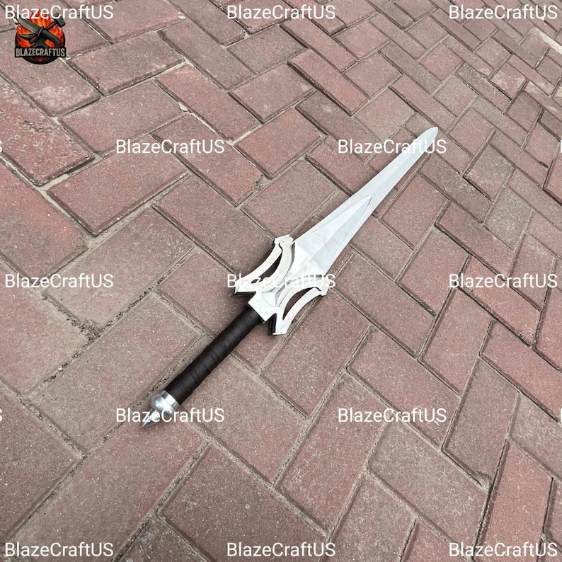May include: A silver and black sword with a stylized hilt and a long, pointed blade. The handle is wrapped in black material. The sword is lying on a brick surface. The text "BlazeCraftUS" is visible in the image.