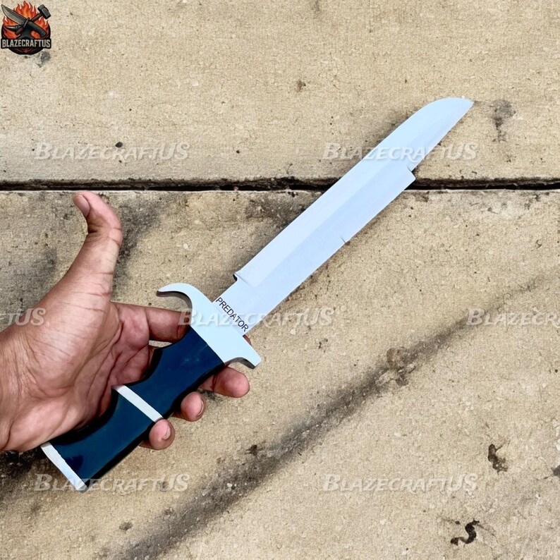 May include: A white and blue knife with a curved blade and a dark blue handle. The word "PREDATOR" is printed on the blade. The knife is held in a hand.