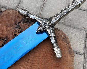 May include: A sword with a bright blue blade featuring a wavy, patterned texture. The hilt is made of metallic silver-toned material with intricate engravings on the handle and a crossguard shaped like a stylized animal head with pointed ears.