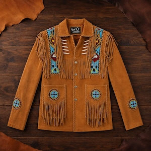 May include: A tan suede jacket featuring long fringe detailing on the chest and pockets. The garment includes blue beaded panels with geometric patterns, white bone-like accents, and circular beaded motifs on the pockets and sleeves.