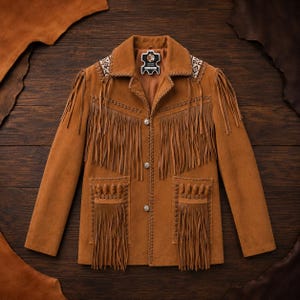 May include: A tan suede leather jacket featuring long fringe detailing across the chest and pockets. The jacket includes a collared neckline, three silver-toned buttons, braided leather trim, and a patterned fabric accent on the shoulders.
