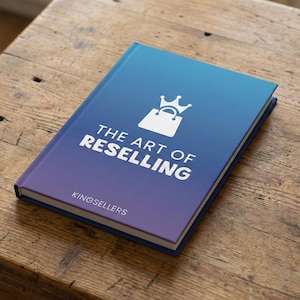 May include: A hardcover book titled "The Art of Reselling" with a blue and purple gradient cover. The cover features a white graphic of a shopping bag with a crown and the text "THE ART OF RESELLING" in white. The book is on a wooden surface.