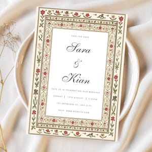 May include: A wedding invitation with a cream background and an ornate border featuring red flowers and green leaves. The text "Sara & Kian" is displayed in elegant script, with event details below. The invitation is set on a white plate.