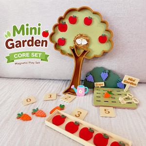 Pode incluir: Um conjunto de jogo magnético Mini Garden Core Set com uma árvore castanha de copa verde-clara, ímanes de maçãs vermelhas e um ninho. Inclui uma horta verde com ímanes de uvas e cenouras, um regador cor-de-rosa e peças numeradas de 0 a 5.