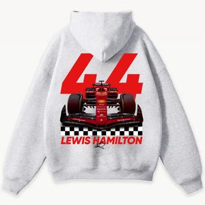 May include: A light gray hoodie featuring a red Formula 1 race car graphic. The number "44" is displayed in large red numerals above the car, with "LEWIS HAMILTON" printed below the car in red. A black and white checkered pattern is at the bottom.