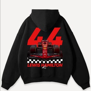 May include: Black hooded sweatshirt featuring a Formula 1 race car graphic. The design includes the number 44 in red, a checkered flag pattern, and the text "LEWIS HAMILTON". The car is red and black.