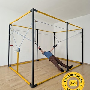 May include: A yellow and black metal frame with blue ropes and pulleys. A person is using the frame for exercise, suspended by straps. The frame has a hand crank and the text "ASK BEFORE BUYING WRITE US" in a yellow circle.