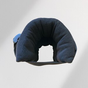 May include: A navy blue travel neck pillow with a curved design. The pillow is made of a soft, plush material and features a blue plastic clasp. The pillow is designed to provide support and comfort during travel.