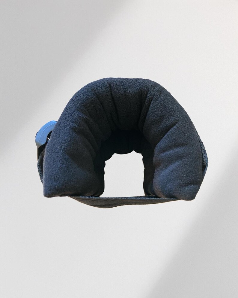 May include: A navy blue travel neck pillow with a curved design. The pillow is made of a soft, plush material and features a blue plastic clasp. The pillow is designed to provide support and comfort during travel.