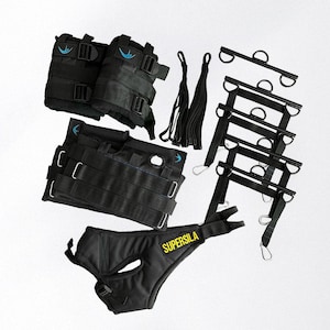 May include: A collection of black fitness equipment, featuring ankle weights, a weight vest, and a hip belt with the word "SUPERSILA" in yellow. Also includes black straps and a ladder-like structure with metal rings.