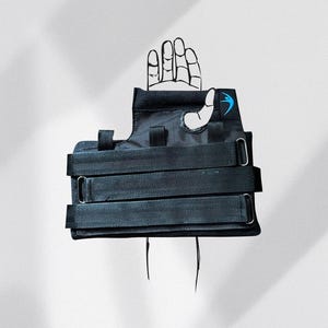 May include: Black wrist brace with three adjustable straps and metal buckles. A blue logo is visible on the brace. A hand illustration is partially visible above the brace.