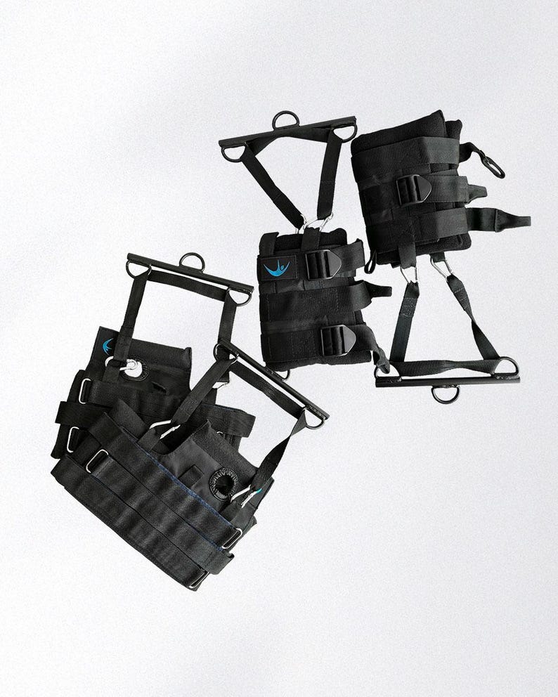 May include: Black inversion therapy equipment with multiple straps, buckles, and metal bars. The equipment has a blue logo and is designed for hanging upside down. The image shows several pieces of the equipment, likely for different body parts.