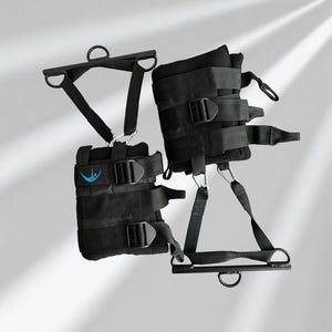 May include: Black inversion boots with multiple adjustable straps and metal D-rings. The boots have a padded interior and a blue logo patch. The design includes a metal bar with a D-ring for hanging. The boots are designed for inversion therapy.