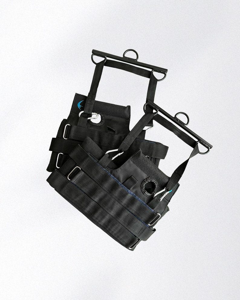 May include: Black exercise equipment with multiple straps, metal rings, and a blue accent. The equipment appears to be designed for suspension training or similar fitness activities. The design includes adjustable straps and metal hardware.