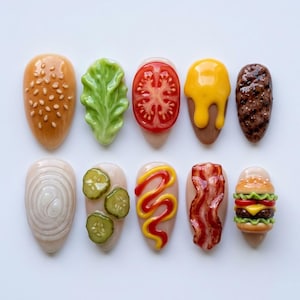 May include: Ten nail art designs, each crafted to resemble a component of a hamburger. The designs include a sesame seed bun, lettuce, tomato, mustard, a burger patty, onion, pickles, bacon, and a miniature burger.