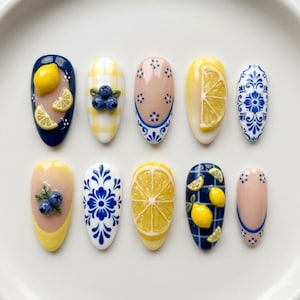 Pode incluir: Uma coleção de dez unhas artificiais em forma de amêndoa com vários designs. Os designs incluem limões, mirtilos e padrões florais em azul, amarelo e branco. Algumas unhas apresentam detalhes de frutas em 3D, outras detalhes pintados intrincados.