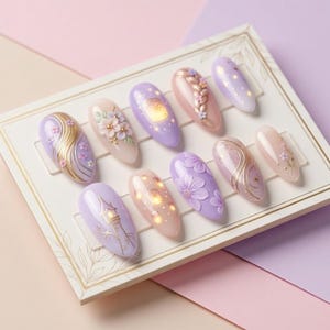 May include: A collection of ten artificial nails with detailed designs. The nails showcase pastel shades like lavender, pink, and peach, with gold and white embellishments. Designs include floral patterns, lanterns, and abstract swirls.