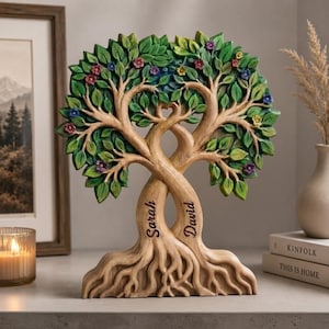 May include: A decorative sculpture of two intertwined trees with light brown trunks and roots. The trunks are engraved with the names Sarah and David. The canopy features green leaves and small colorful flowers in shades of red, blue, and yellow.