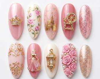 Peut inclure: Dix faux ongles avec divers motifs. Les ongles présentent différentes nuances de rose, des décorations dorées et des paillettes. Les motifs incluent une couronne, des roses, un château, un rouet et une princesse.