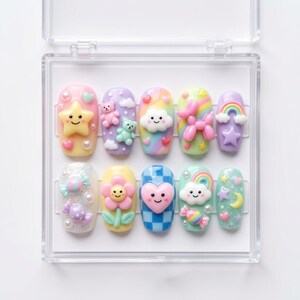 Pode incluir: Um conjunto de dez unhas postiças numa caixa de plástico transparente, com cores pastel e berloques 3D incluindo estrelas sorridentes, ursinhos, nuvens, arco-íris, animais de balão, flores, corações, doces e luas com brilho e pérolas.