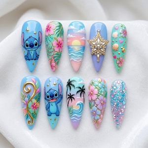 Op de afbeelding: Een set van tien amandelvormige kunstnagels met diverse ontwerpen. De ontwerpen omvatten stripfiguren, tropische bloemen, zonsondergangen en oceaanthema's. Kleuren zijn blauw, roze, groen en goud. Sommige nagels hebben glitter en versieringen.