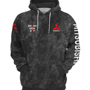 Może przedstawiać: Czarna i szara bluza z kapturem z teksturowanym wzorem. Bluza z kapturem zawiera napis "BRAND NEW DAY" i logo Mitsubishi w kolorze czerwonym. Słowo "MITSUBISHI" jest wydrukowane pionowo na prawym rękawie.