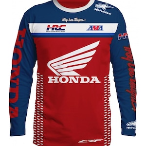 Puede incluir: Jersey de motocross de manga larga rojo, blanco y azul con el logotipo de Honda y el texto "HRC Honda Racing" y "AMA". El jersey también presenta el texto "Troy Lee Designs" en la parte delantera y trasera.