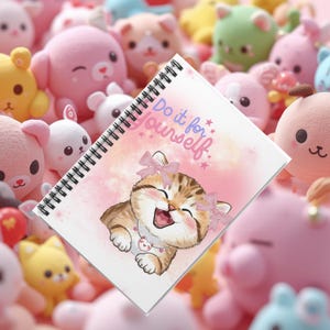 May include: A spiral-bound notebook with a white cover featuring a pink watercolour background and a cartoon illustration of a smiling tabby kitten wearing two pink bows and a heart-shaped pendant. The text Do it for yourself is printed in blue and pink.
