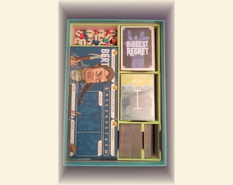 Pode incluir: Uma caixa de jogo de tabuleiro com vários componentes. A caixa contém dados, cartas com o texto "BIGGEST REGRET" e tabuleiros de jogo. O jogo apresenta ilustrações e texto, incluindo o nome "BERT" e escalas numéricas.