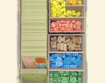 Pode incluir: Um organizador de jogos de tabuleiro de madeira com peças de jogo em forma de animais amarelos, rosa, castanho, azul e verde. O organizador também contém uma pilha de cartas verdes e brancas ilustradas.