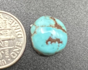 Puede incluir: Una piedra preciosa turquesa en cabujón con vetas marrones, junto a una moneda de diez centavos de dólar estadounidense. La turquesa es de color azul claro y tiene una superficie lisa y pulida.