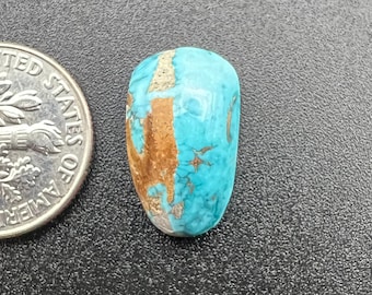 Puede incluir: Un cabujón turquesa con matriz marrón. La piedra es de color azul claro con vetas marrones que la atraviesan. La piedra es aproximadamente del tamaño de una moneda de euro.