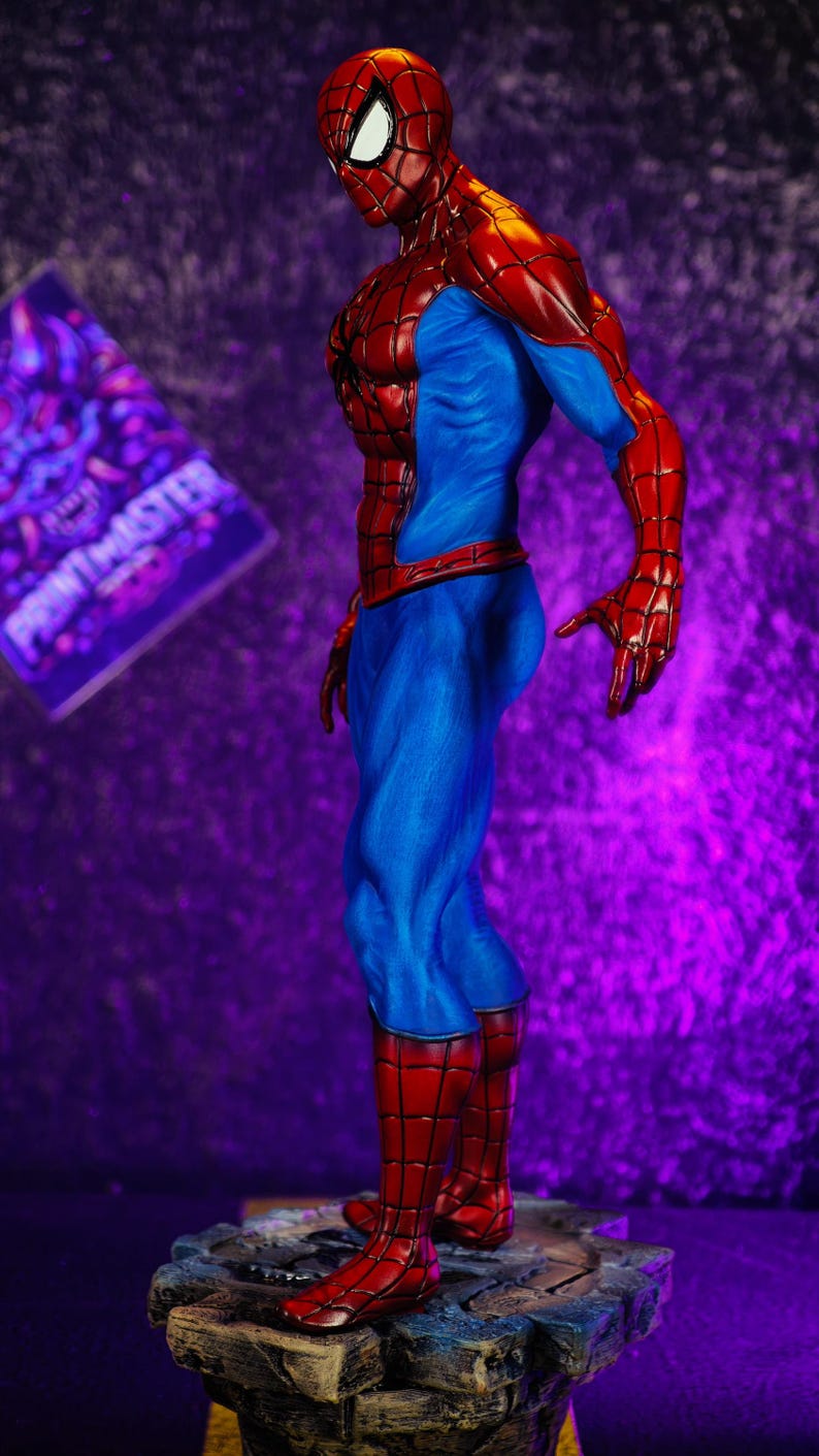 Puede incluir: Una figura detallada de Spider-Man en una pose din&aacute;mica. La figura es predominantemente roja y azul, con un patr&oacute;n de telara&ntilde;a texturizado en las secciones rojas. La base es una superficie rocosa y texturizada. El fondo es un degradado de p&uacute;rpura.