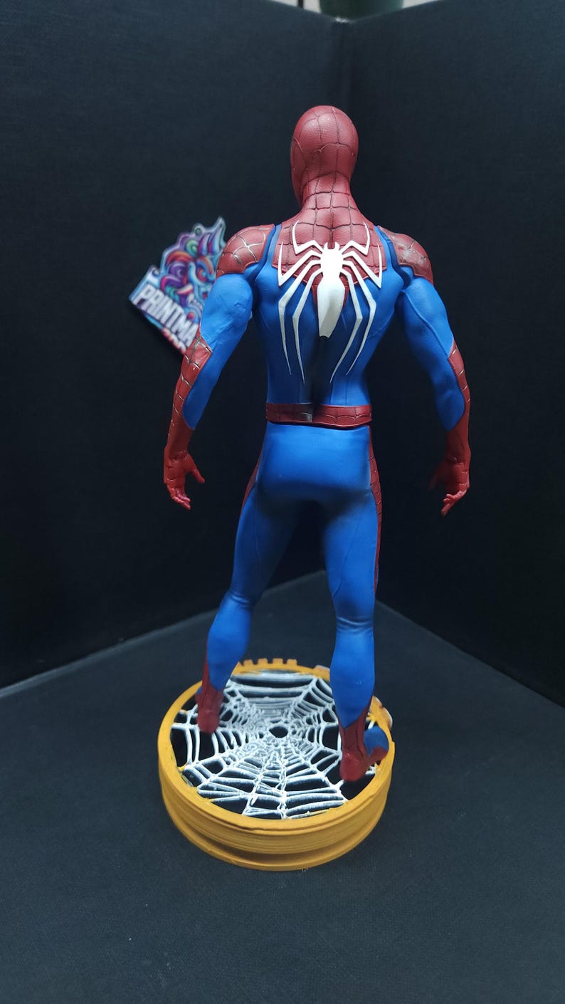 May include: A red and blue action figure of Spider-Man standing on a web-shaped base. The figure is posed with its back to the camera, showing the white spider symbol on its back.