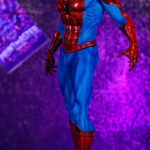 Puede incluir: Figura detallada de Spider-Man en una pose din&aacute;mica. La figura es predominantemente roja y azul, con un patr&oacute;n de telara&ntilde;a en las secciones rojas. La figura se alza sobre una base texturizada detallada, sobre un fondo p&uacute;rpura.