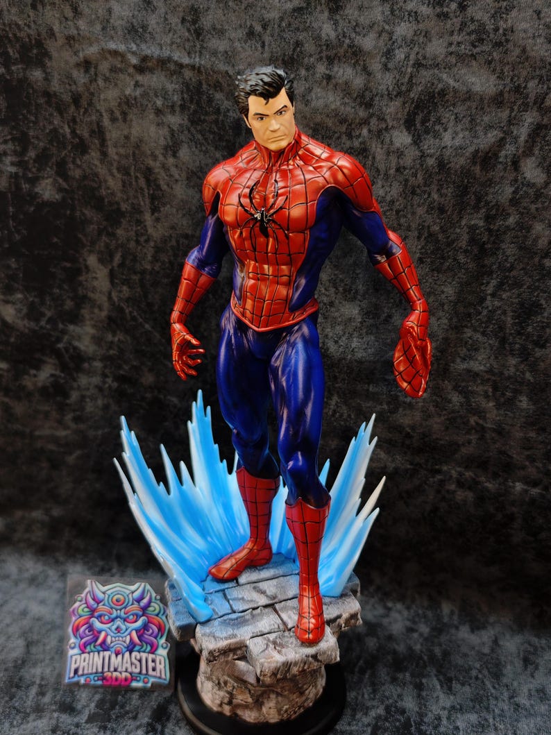 Op de afbeelding: Een gedetailleerd beeldje van Spider-Man in een dynamische pose, met zijn iconische rood-blauwe pak. Het beeldje staat op een rotsachtige basis met blauwe energie-effecten en heeft een zwart spinnenembleem op de borst. De basis bevat het "PRINTMASTER" logo.