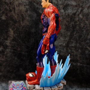 Op de afbeelding: Gedetailleerd beeldje van Spider-Man in een dynamische pose, met zijn iconische rood-blauwe pak. Het beeldje staat op een stenen basis met blauwe watereffecten. Het beeldje heeft een gedetailleerd gezicht en is een verzamelobject.