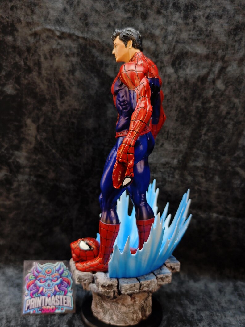 Op de afbeelding: Gedetailleerd beeldje van Spider-Man in een dynamische pose, met zijn iconische rood-blauwe pak. Het beeldje staat op een stenen basis met blauwe watereffecten. Het beeldje heeft een gedetailleerd gezicht en is een verzamelobject.