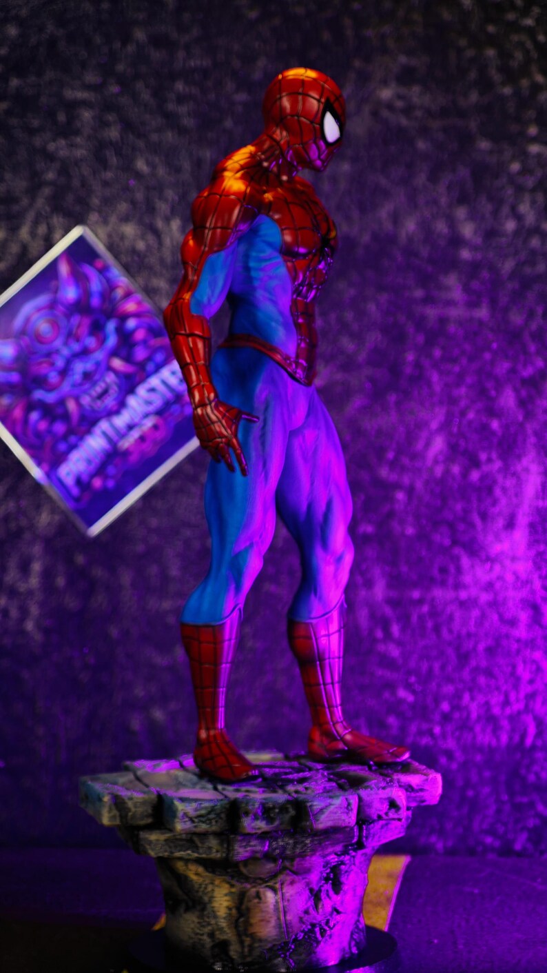 Puede incluir: Una figura detallada de Spider-Man en una pose cl&aacute;sica, con un traje rojo y azul. La figura est&aacute; sobre una base de piedra. Un letrero con el texto "PRINTMASTER" est&aacute; en el fondo.
