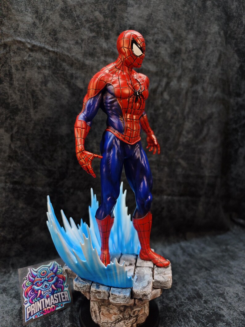 Op de afbeelding: Gedetailleerd beeldje van Spider-Man in een dynamische pose, met zijn iconische rood-blauwe pak. Het beeldje staat op een rotsachtige basis met een gestileerd watereffect. Het Printmaster-logo is zichtbaar.
